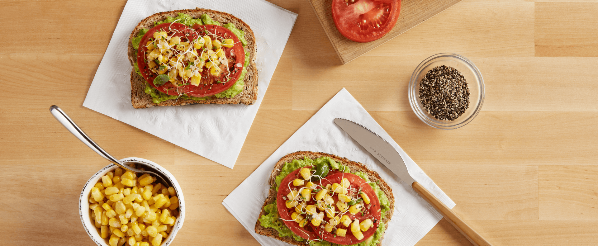 Sliced bread with avocado, tomatoes and corn on top of a Vanity Fair Everyday Napkin.