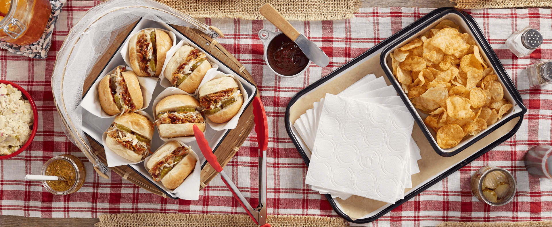 Picnic table with chips and barbecue sandwiches along side Vanity Fair Napkins.