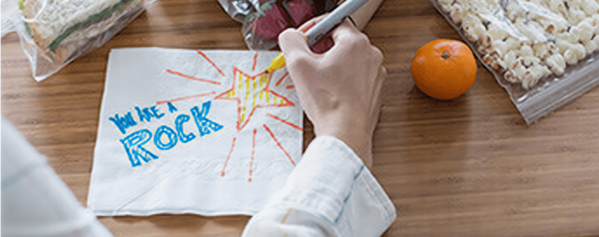 Someone drawing a message on a napkin that reads You Are a Rock.