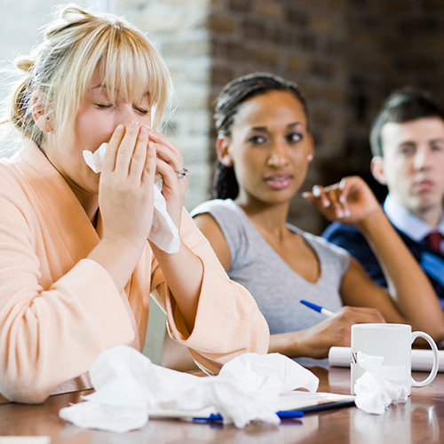 Woman sneezing at a table with coworkers.
