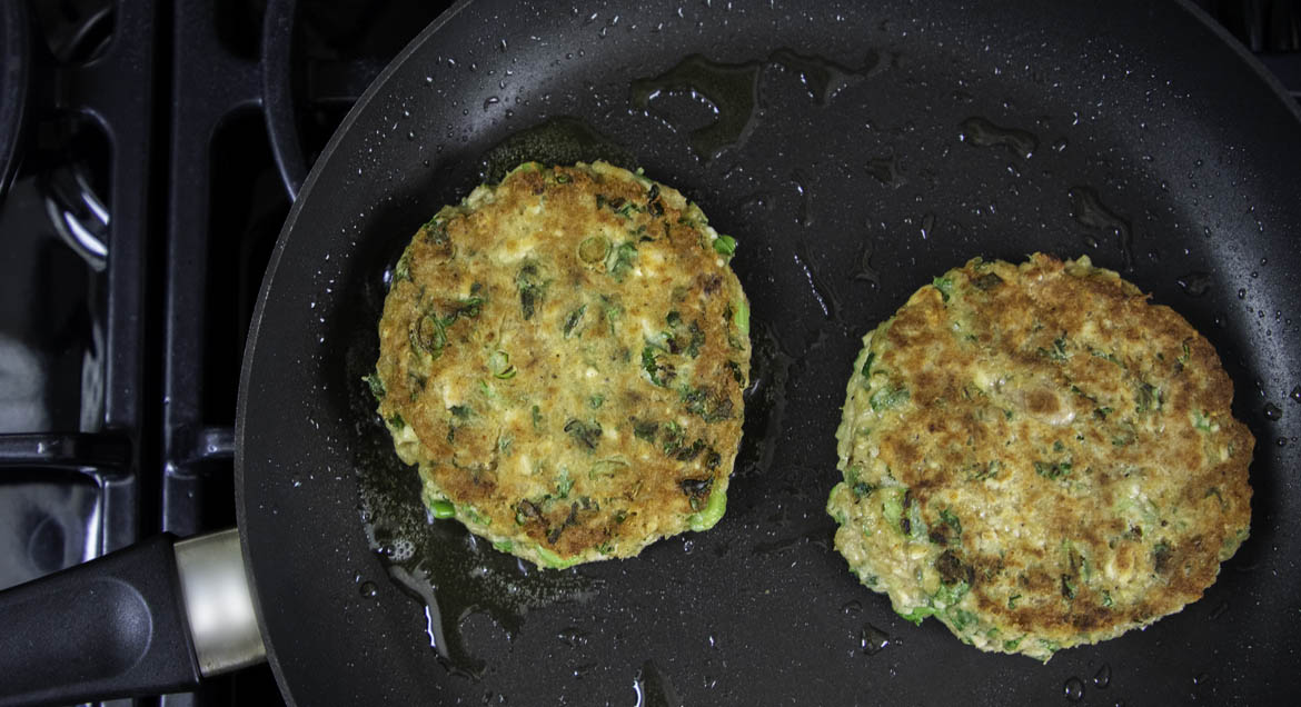 Salmon Burger Patties In Black Frying Pan.