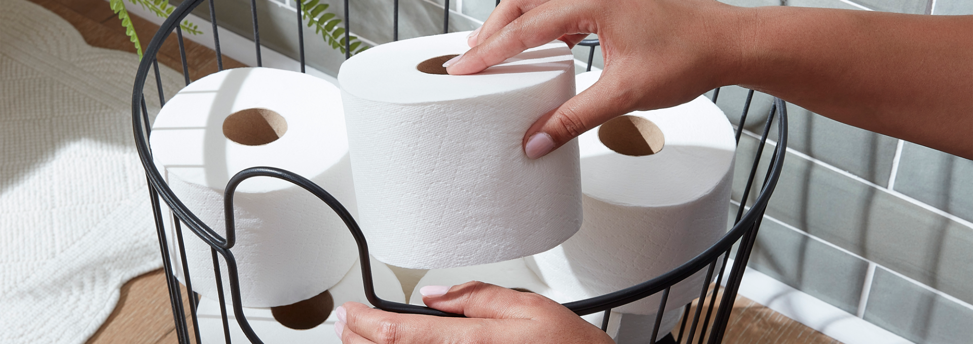 A person placing a Quilted Northern toilet tissue roll into a basket.