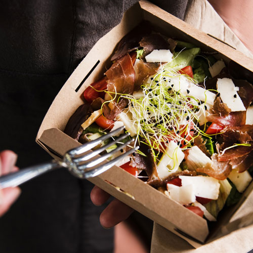 Patron eats salad from a sustainable brown container.