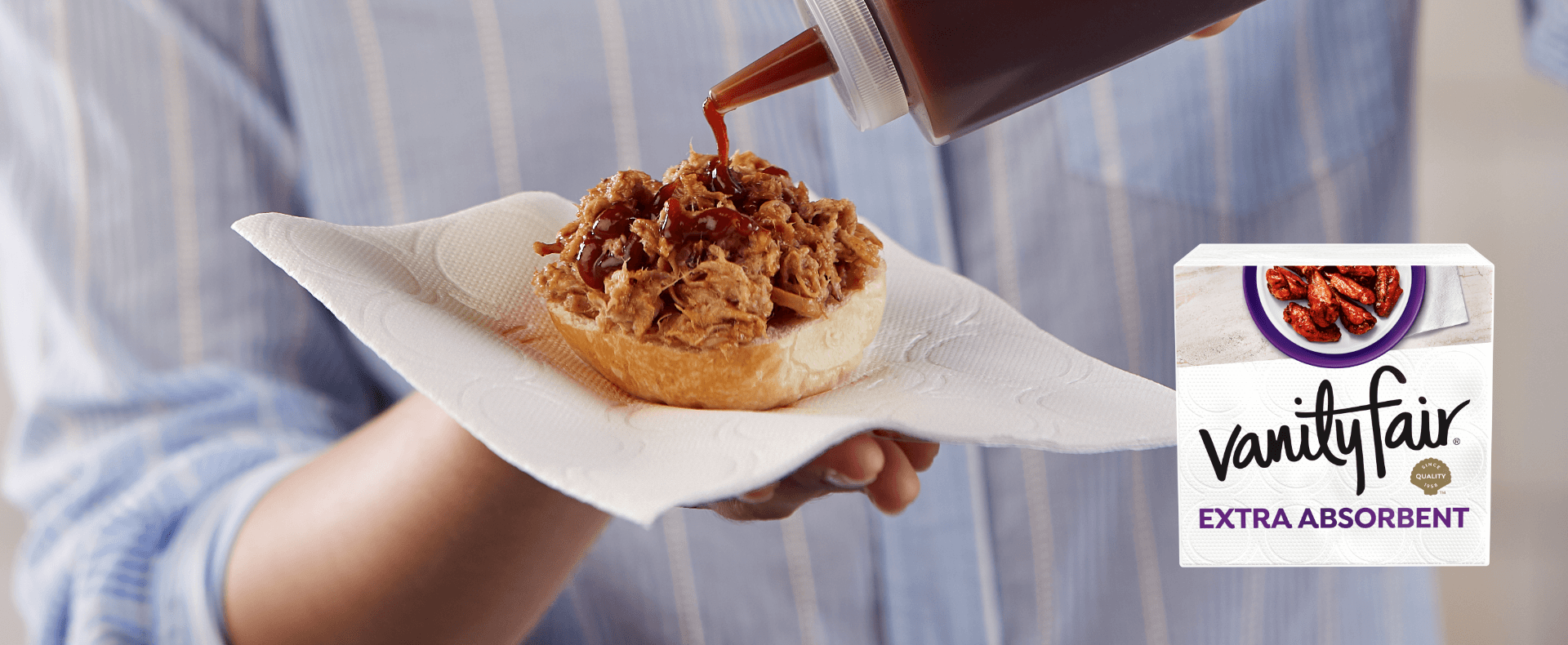 Someone holding a BBQ pork sandwich on a Vanity Fair Extra Absorbent napkin.